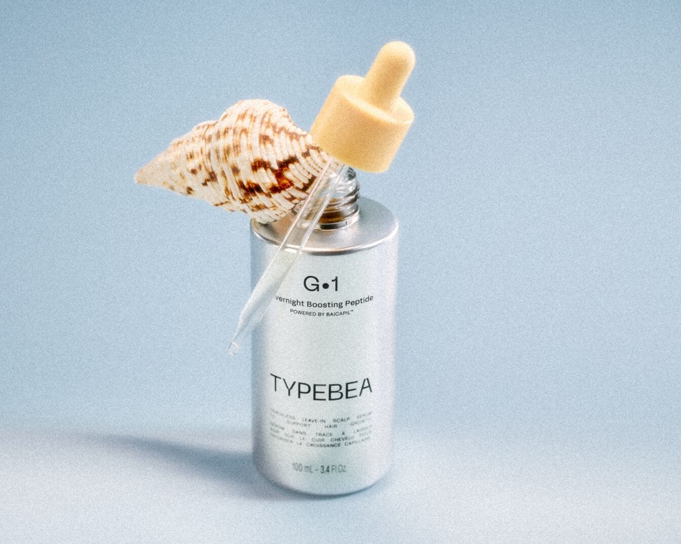 TYPEBEA G&bull;1 Overnight Boosting Peptide pudeli l&auml;hivaade pipetiga ja helesinisel taustal oleva merekarbiga. Pudel lubab kerget pealej&auml;etavat hoolitsust, et toetada juukseid ja peanahka.
